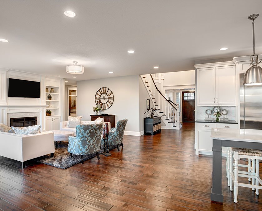 Living room with white furniture, white couches, gray carpet, big watch on the wall, flat screen TV, fireplace, laminate floor, and open space kitchen.