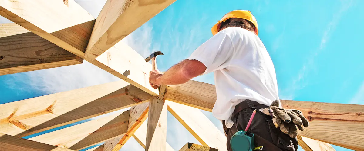 Low-angle view of man hammering on a stick frame roof