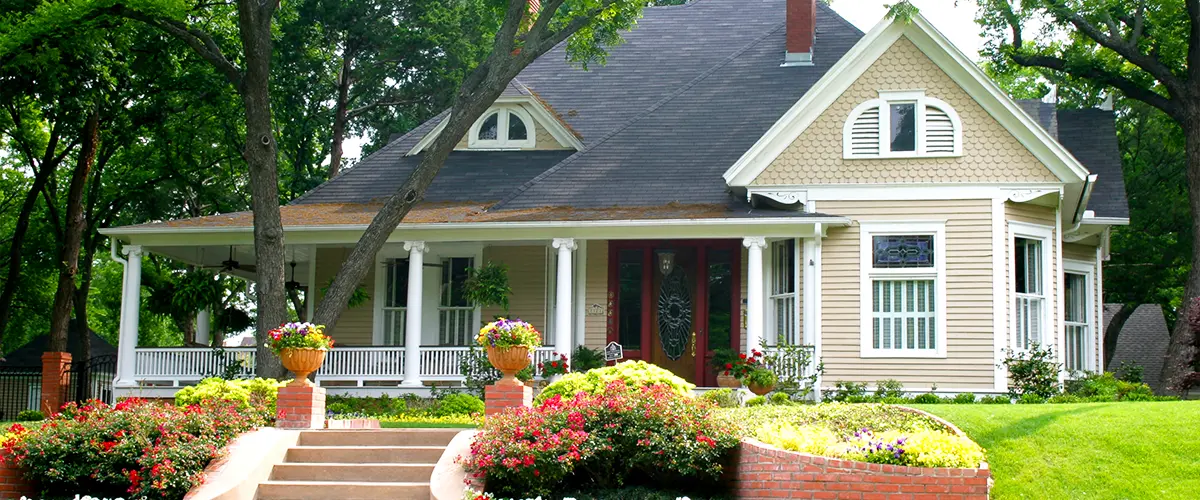 Beautiful historic home with lush landscaping and colorful flower beds, featuring a large front porch and mature trees.