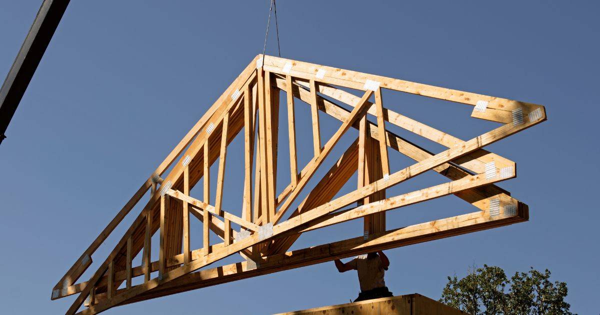 Large wooden roof truss being lifted by a crane during construction installation