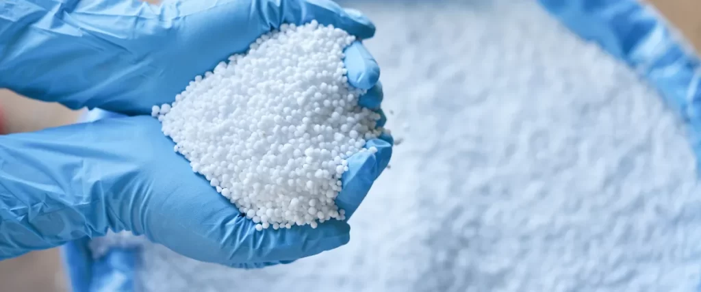 Person wearing blue gloves holding a handful of small white resin granules.