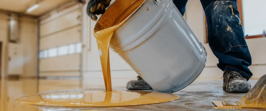 Yellow epoxy resin being poured from a bucket onto the floor for coating application.