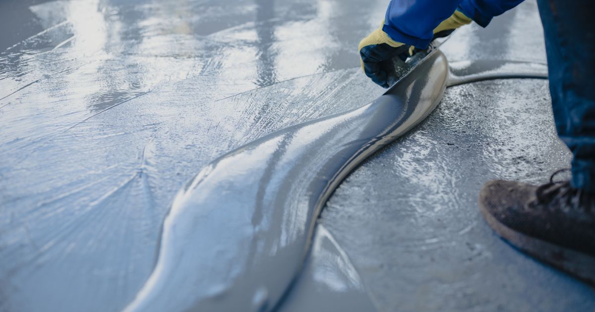 Worker spreading self-leveling epoxy coating on a floor with a trowel.