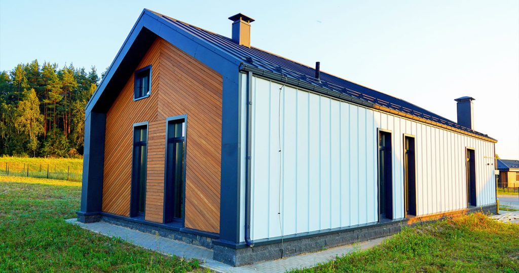 Barndominium with wood and metal siding, black roof, and tall windows in a rural landscape with trees