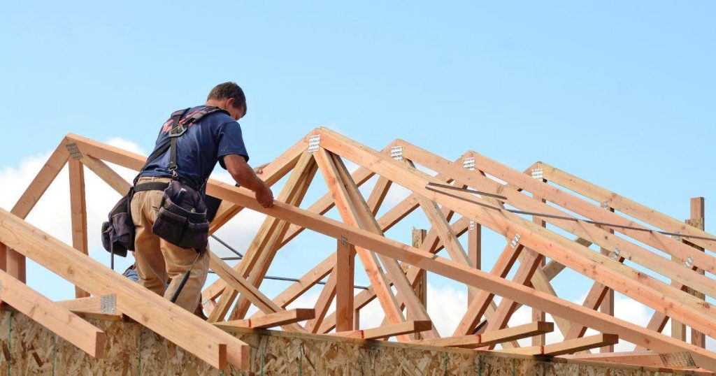A construction worker installing wooden roof trusses on a house under construction (selected).